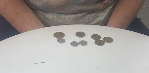 A person sits at a white table with eight assorted coins spread out in front of them, suggesting a quiet moment of...